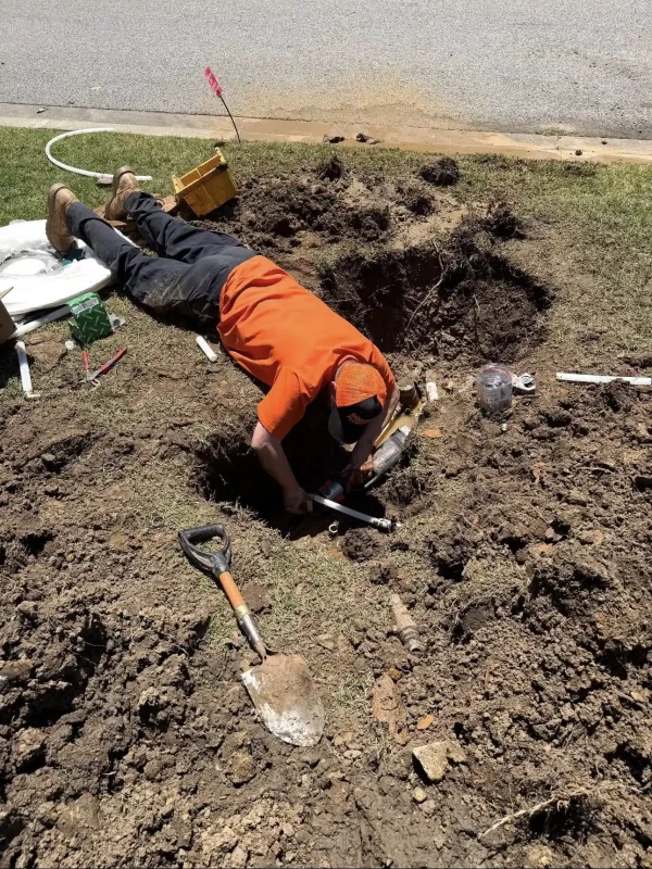A clean-cut Wooten Plumbing team member working carefully inside a dirt excavation to repair an underground water main line, providing certified plumbing Sapulpa services