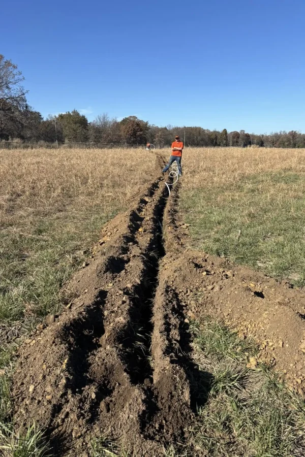 Wooten Plumbing team trenching out new water pipe in pasture